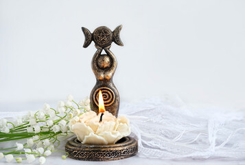 amulet of Triple Goddess figurine, floral candle and lilies of the valley flowers close up,...