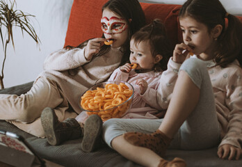 Three girls are watching a movie sitting on the couch.