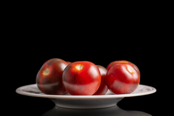 Several ripe black cherry tomatoes on a white ceramic plate, macro, isolated on black background.