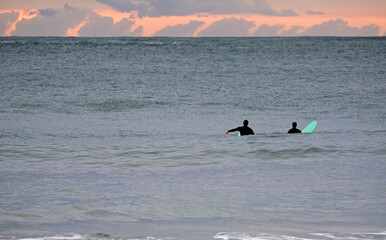 Two surfers waiting for the perfect wave during sunset in Spain