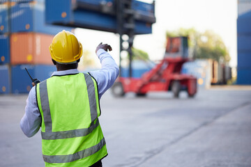 back view African worker or engineer using walkie talkie and showing gesture to crane car in...