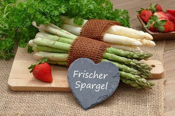 Weißer und grüner frischer Spargel auf einem Holzbrett mit Erdbeeren.