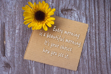 Motivational on brown note with gerbera yellow flower on wooden surface.