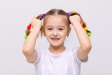 The little girl lifts her braids of hair up, with multi-colored elastic bands, and smiles broadly....