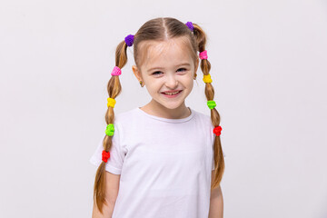 The little girl with braids of hair with multi-colored elastic bands, smiles broadly. Hairstyles...