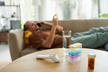Pills and contactless thermometer on table of sick man calling doctor