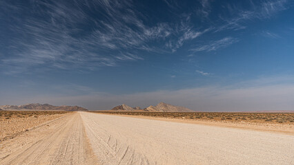 Straße im Namib-Naukluft Nationalpark, unendliche Weite, in Hintergrund Gebirge - obrazy, fototapety, plakaty