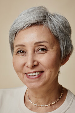 Head of happy aged woman with grey short hair and toothy smile looking at camera during photo shooting against beige background