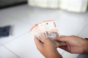 A woman's hand holds five thousand Indonesian notes for the Eid al-Fitr holiday