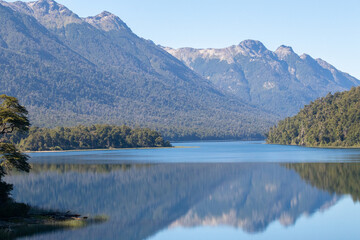 Calm and relaxing horizontal view of mountain range full of dense forests reflecting onto a lake's...