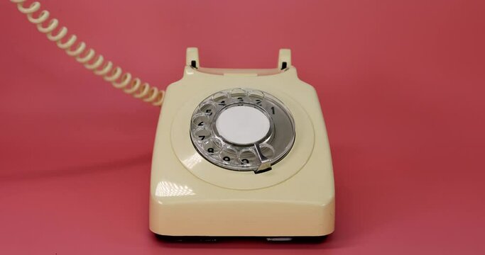 An old retro style British telephone with the receiver being picked up and put down again by a mans hand on a pink background
