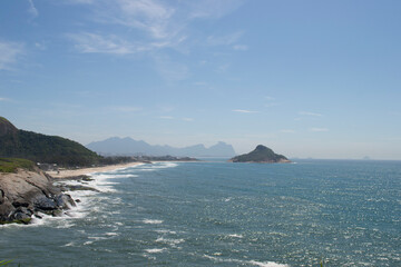 Mountains, vegetation and the ocean with clear blue waters of Praia de Grumari, located in the city of Rio de Janeiro.