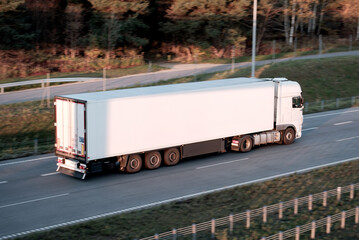 Modern white semi-trailer trucks on the highway driving in the right lane. Commercial vehicle for shipping and post delivery. Shipping of the goods on land with a door-to-door delivery process..