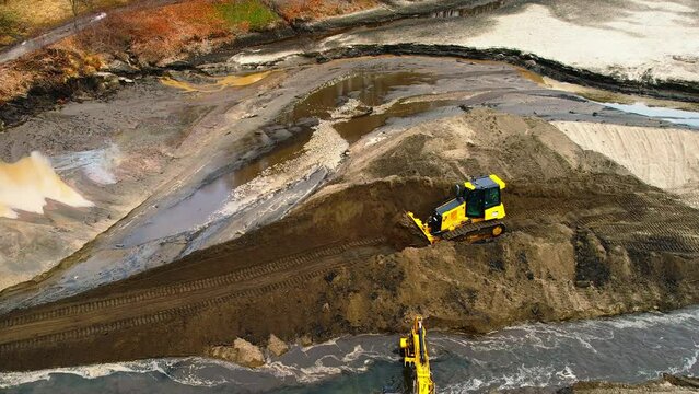 Aerial tracking shot yellow Bulldozer pushing earth on new dirt road on the bank of a small river