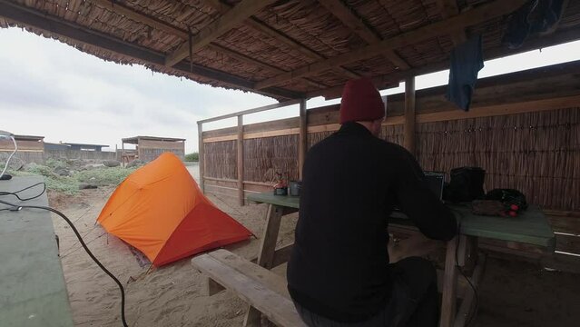 Time lapse: Man at camp site types on laptop on picnic table by tent