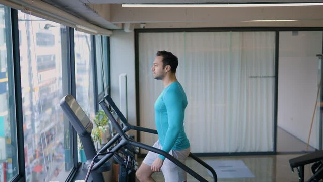 Fit Male Exercises on Stepmill Stair Climber Machine in Modern Gym While Enjoying City Street View Through Window - Medium Wide
