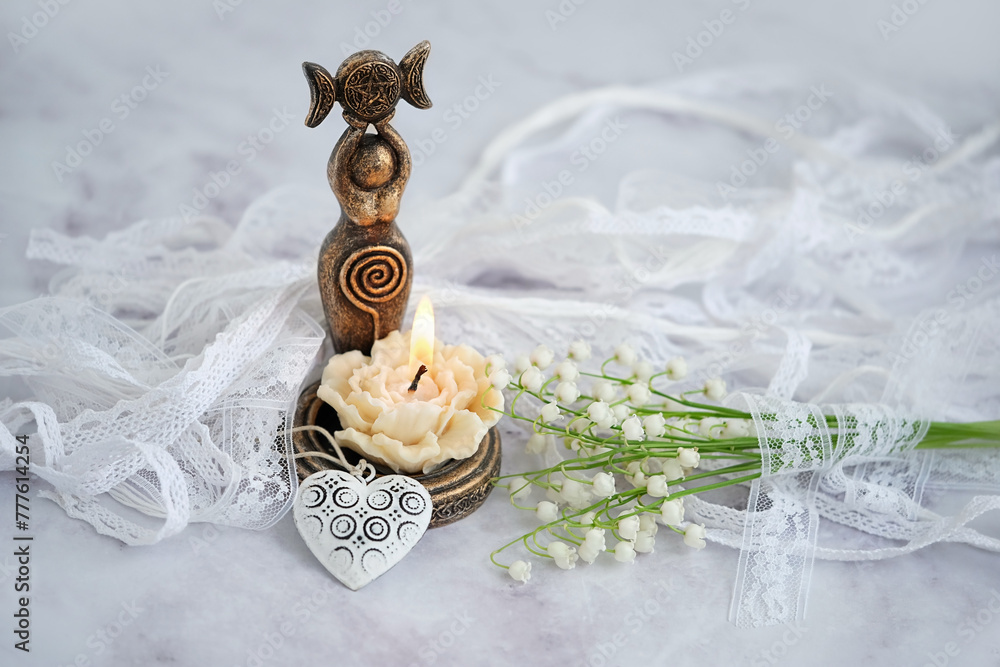 Poster amulet of triple goddess figurine, floral candle and lilies of the valley flowers close up, abstract