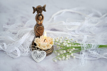 amulet of Triple Goddess figurine, floral candle and lilies of the valley flowers close up,...