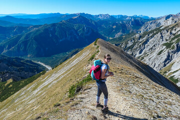 Hiker woman on idyllic hiking trail on alpine meadow with scenic view of majestic Hochschwab mountain range, Styria, Austria. Wanderlust in remote Austrian Alps. Sense of escapism, peace, reflection - obrazy, fototapety, plakaty