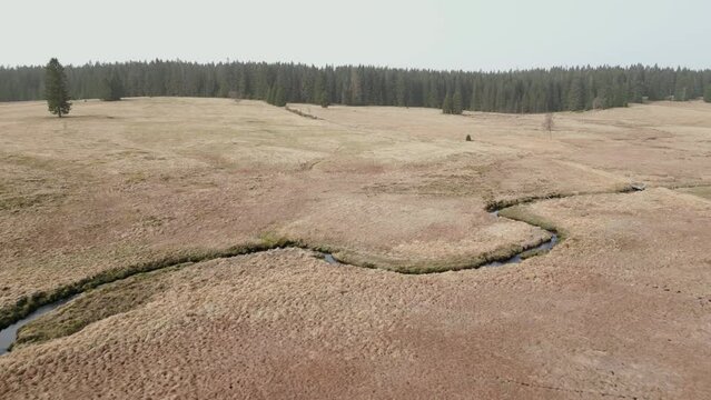 Landscape of Kruse Hory features an open field with patches of grass, a winding stream, and a distant forest under a clear sky.
