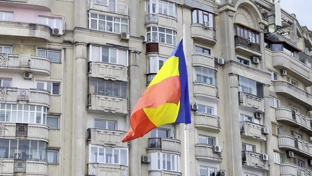 Romania national flag on a windy day with worn out, gray communist blocks for the middle class, as a background