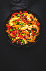 Hot stir fry shrimps with colorful paprika, green peas, chives and sesame seeds with ginger, garlic and soy sauce.   Black kitchen table background, top view