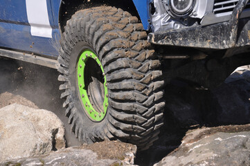 Blue off-road car crossing a rocky trail, a tire deformed by the force of climbing a rock