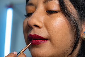 latina woman painting her lips with a red brush - beauty concept
