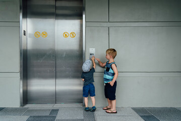 Rear view of two small boys waiting for elevator and pushing button