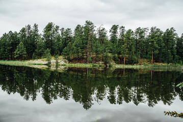 Fototapeta na wymiar Wide view of lake with reflection of evergreen trees and sky