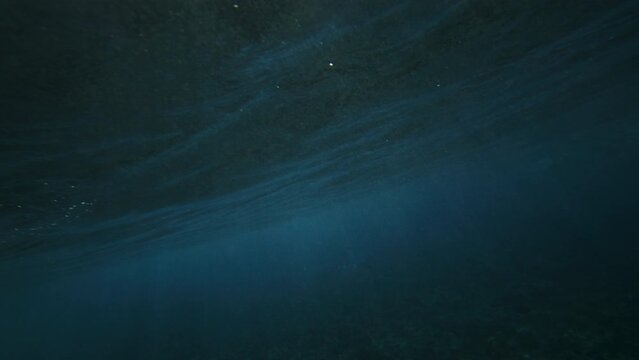 Moody grey rubble coral reef with ocean water glistening and shining as wave creates barrel, view from behind