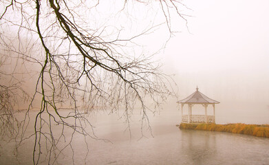 Foggy day in the park with a gazebo by the lake.