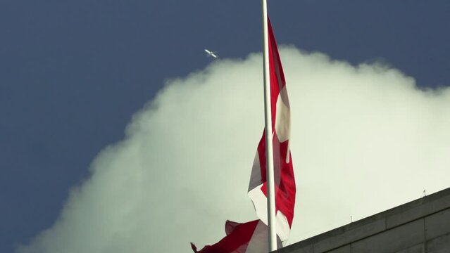 Slow-motion shot of the waving Canadian flag with an airplane passing by in the background.