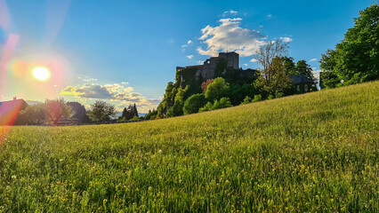 Warm sun beams through Idyllic alpine meadow during sunset with scenic view of Finkenstein Castle...