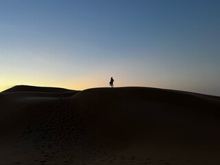 man on dunes silhouetted against sky at sunset, outdoors