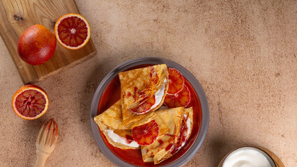 Traditional French Crepes suzette pancakes with bloody orange on light beige background decorated...
