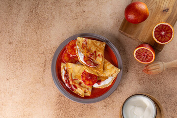 Crepes stuffed with ricotta and bloody orange on warm beige background. Thin pancakes, blini. Sweet dessert.