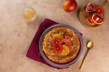 Crepes with ricotta cheese and bloody orange on beige pastel background, copy space. Delicious crepes, thin pancakes.
