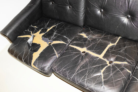 Broken leather sofa with cracks and holes with hard direct flashlight