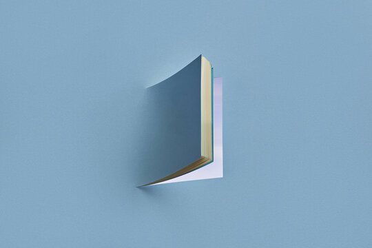 Papercraft book open as window on blue studio background.