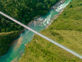 Aerial view of a Tibetan suspended bridge in Nepal is a primitive type of bridge in which the deck lies on two parallel load-bearing cables that are anchored at either end. Wild nature - 777643278
