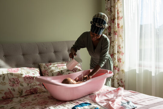 Smiling mother washing baby in bath in bedroom 