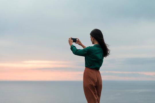 Standing woman taking pictures during scenic sea sunset