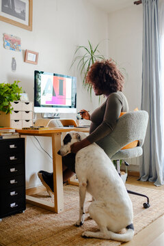 Pregnant designer woman in home office petting her dog
