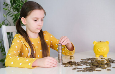 Happy girl counts money coins, puts money in pile. Child learns financial responsibility and saves...