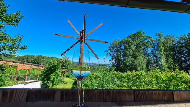 Wine tasting on vineyards and windmill klapotetz in Ehrenhausen an der Weinstrasse, Leibnitz, South Styria, Austria. Drinking glass of white wine on idyllic winery stretching over lush green hills