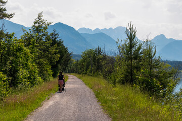 Woman with baby carriage on idyllic hiking trail along Drava river. Scenic view of mountain peaks...