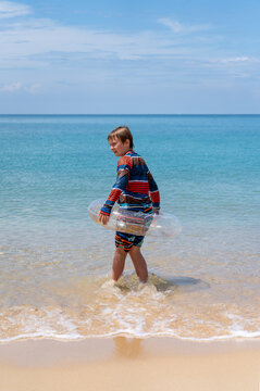 boy in inflatable ring stands in front of sea