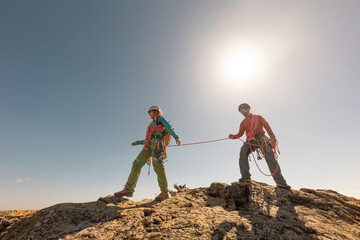 Two people are climbing a mountain together, one of them is holding a rope. Scene is adventurous...