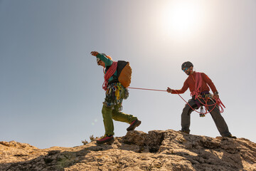 Two people are climbing a mountain together, one of them is holding a rope. Scene is adventurous...